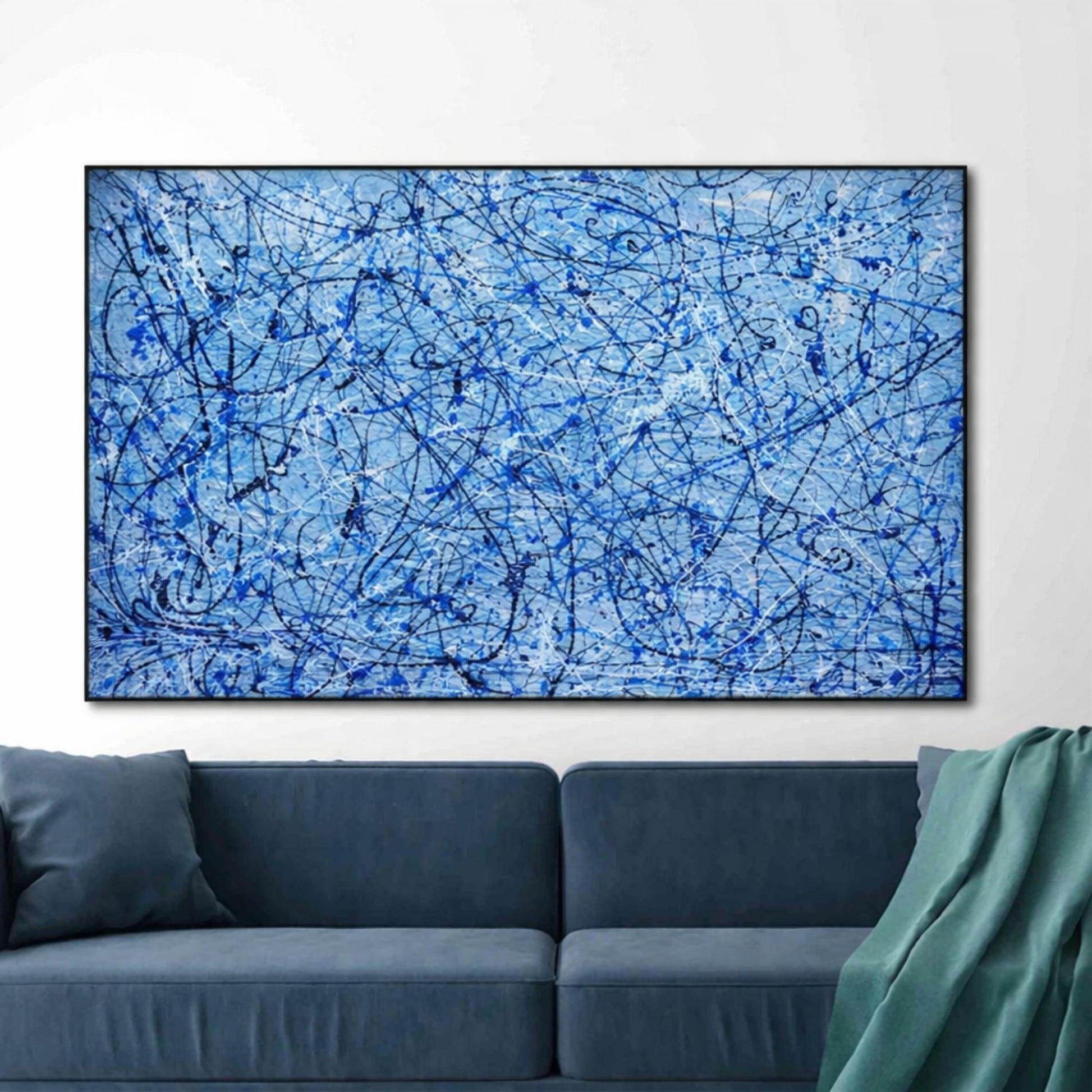 Blue abstract drip painting with black and white splashes framed above modern sofa