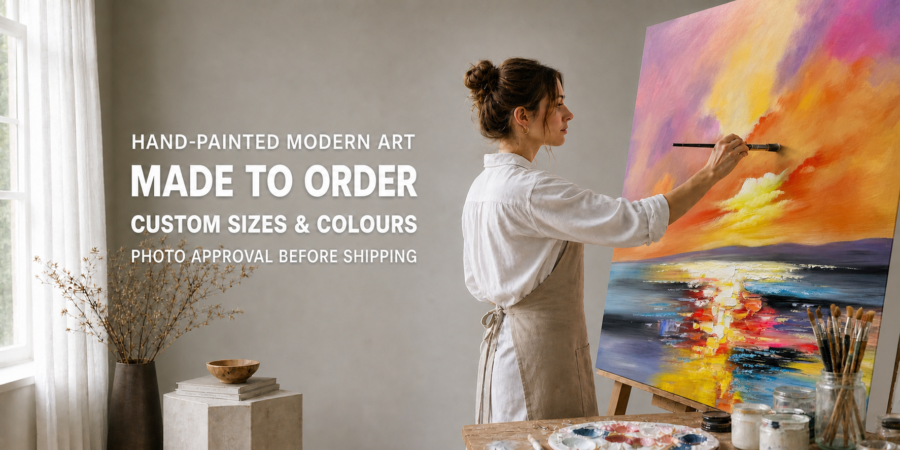 A woman in a white shirt and beige apron paints a colorful landscape scene on a canvas easel in a bright studio. Text on the left reads 'HAND-PAINTED MODERN ART MADE TO ORDER CUSTOM SIZES & COLOURS PHOTO APPROVAL BEFORE SHIPPING'.