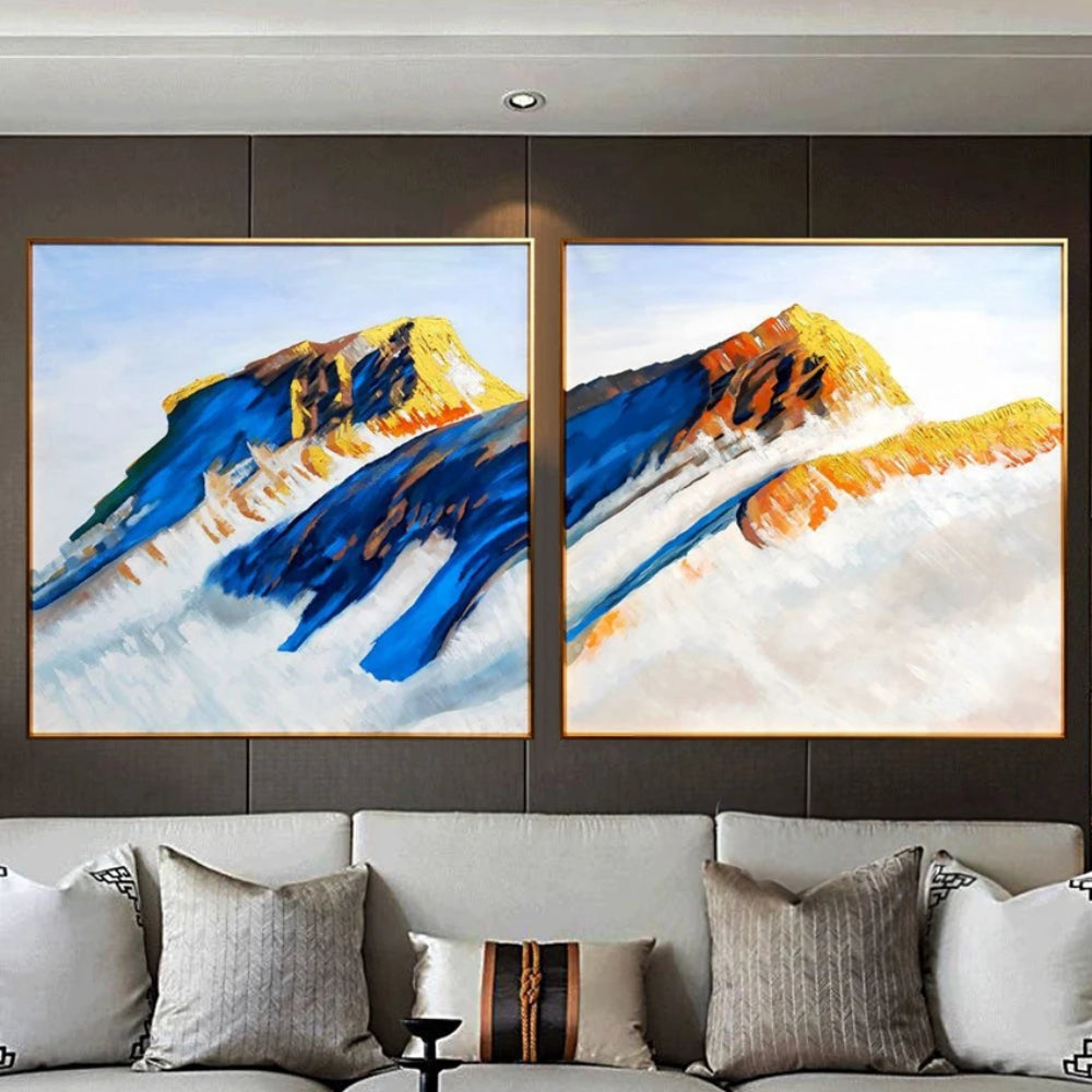 Room mockup showing two mountain paintings with deep blue slopes and ochre peaks rising above broad pale white areas.