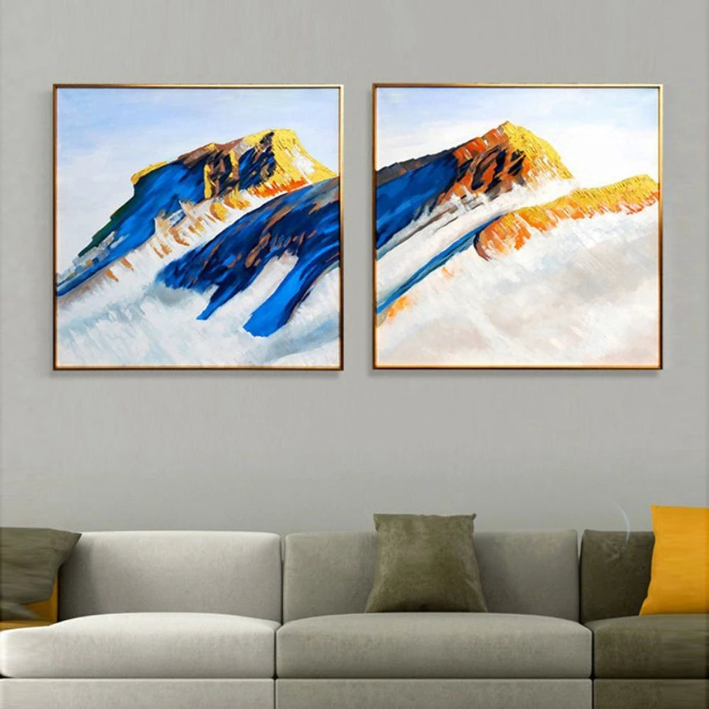 Room mockup showing two mountain paintings with deep blue slopes and ochre peaks rising above broad pale white areas.