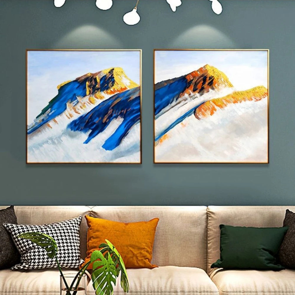 Room mockup showing two mountain paintings with deep blue slopes and ochre peaks rising above broad pale white areas.