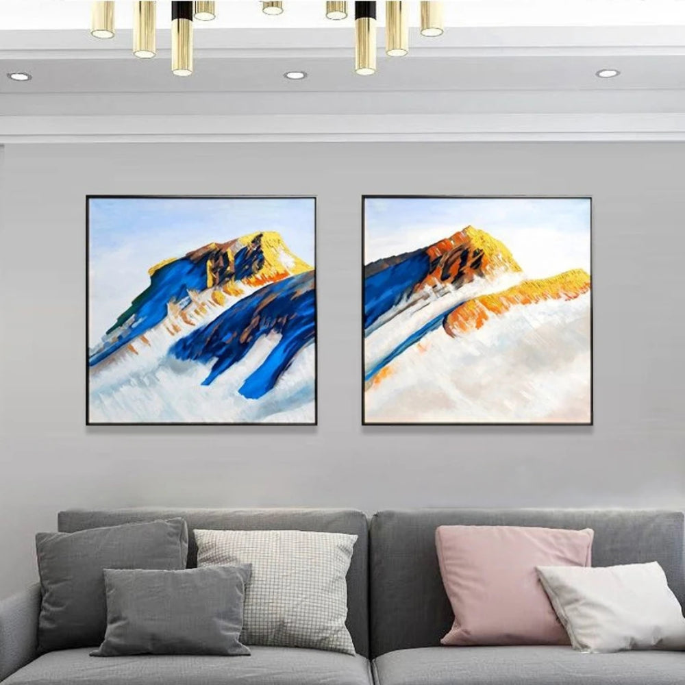 Room mockup showing two mountain paintings with deep blue slopes and ochre peaks rising above broad pale white areas.