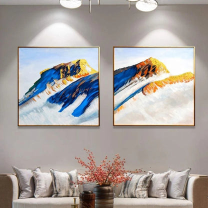 Room mockup showing two mountain paintings with deep blue slopes and ochre peaks rising above broad pale white areas.