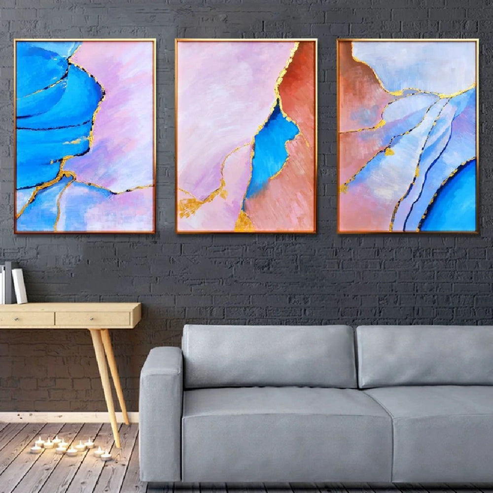 Room mockup showing three abstract panels with vivid blue, pale pink and coral flowing fields divided by thin gold-coloured lines.
