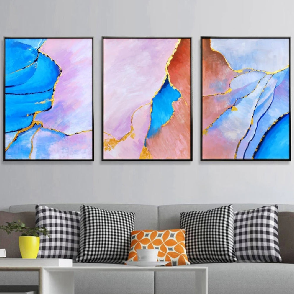 Room mockup showing three abstract panels with vivid blue, pale pink and coral flowing fields divided by thin gold-coloured lines.