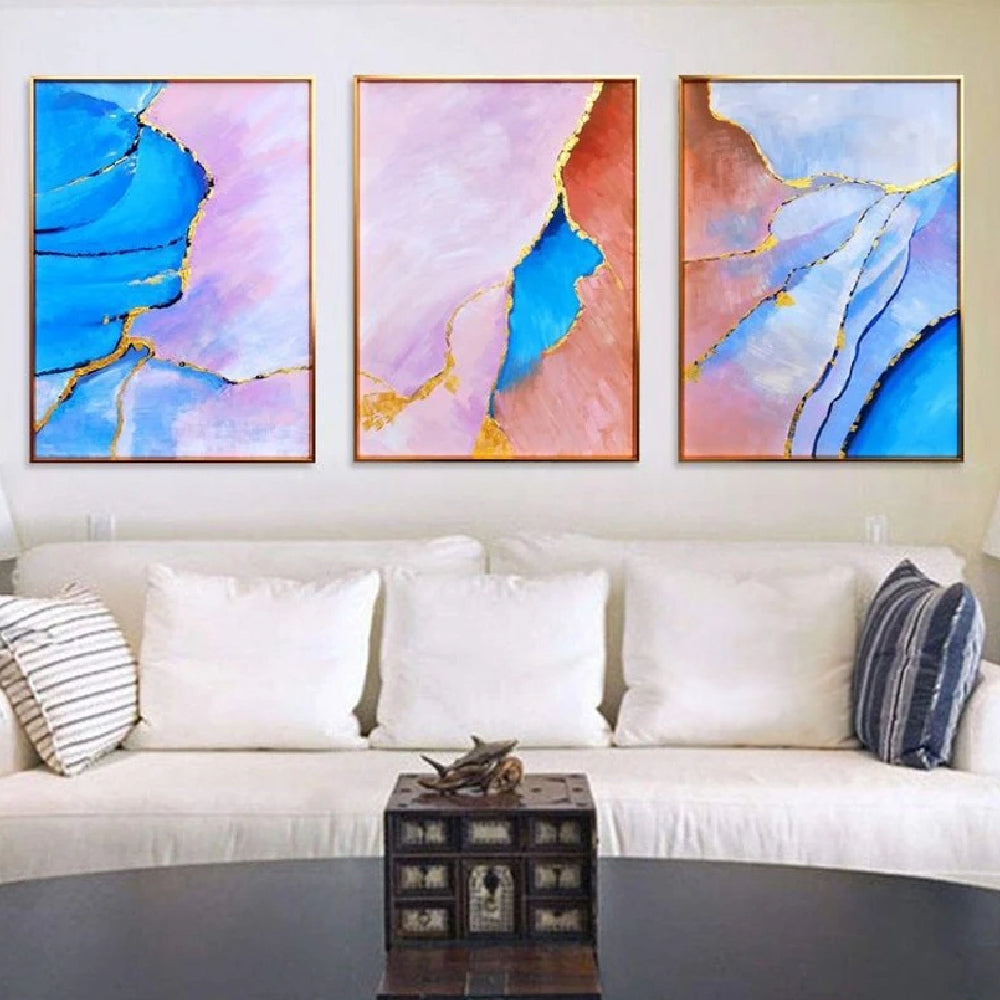 Room mockup showing three abstract panels with vivid blue, pale pink and coral flowing fields divided by thin gold-coloured lines.