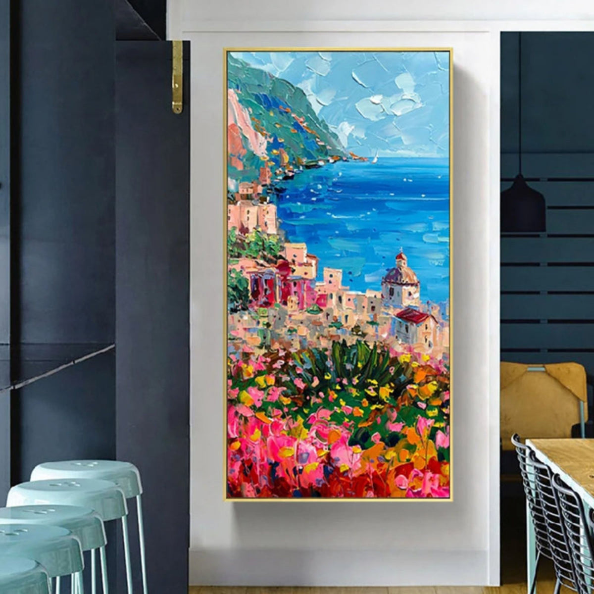 Room mockup showing bright blue sea beside a hillside town with pastel buildings and pink, orange and yellow foreground flowers.