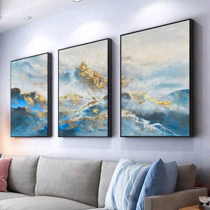 Room mockup showing three blue and white abstract mountain-like landscapes with gold-coloured textured peaks and sweeping water-like bands.