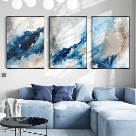 Room mockup showing three abstract panels with deep blue flowing bands through cloudy white, pale blue and grey textured fields.