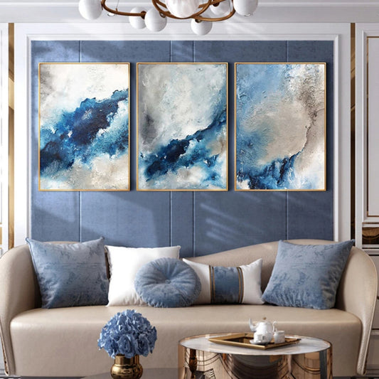 Room mockup showing three abstract panels with deep blue flowing bands through cloudy white, pale blue and grey textured fields.