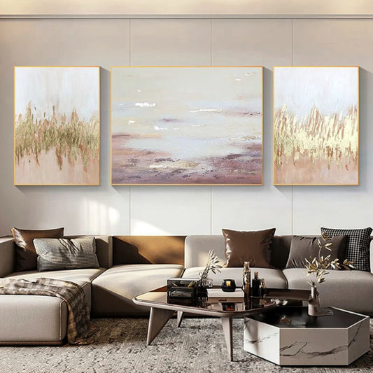 Room mockup showing three pale blush and cream abstracts with gold-coloured textured marks; the centre has soft horizontal mauve bands.