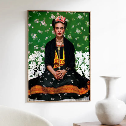 Framed portrait of a woman with floral headpiece on a floral background, placed on a white wall next to a white vase.