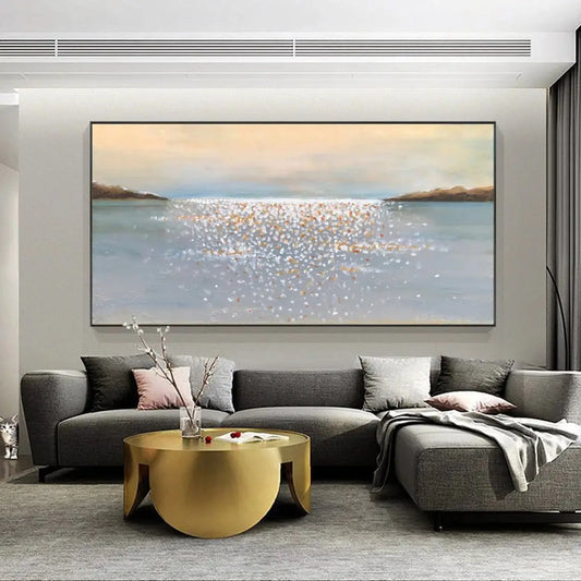Room mockup showing pale blue-grey water with small cream and gold-coloured reflective dabs between distant dark shores beneath a peach-grey sky.