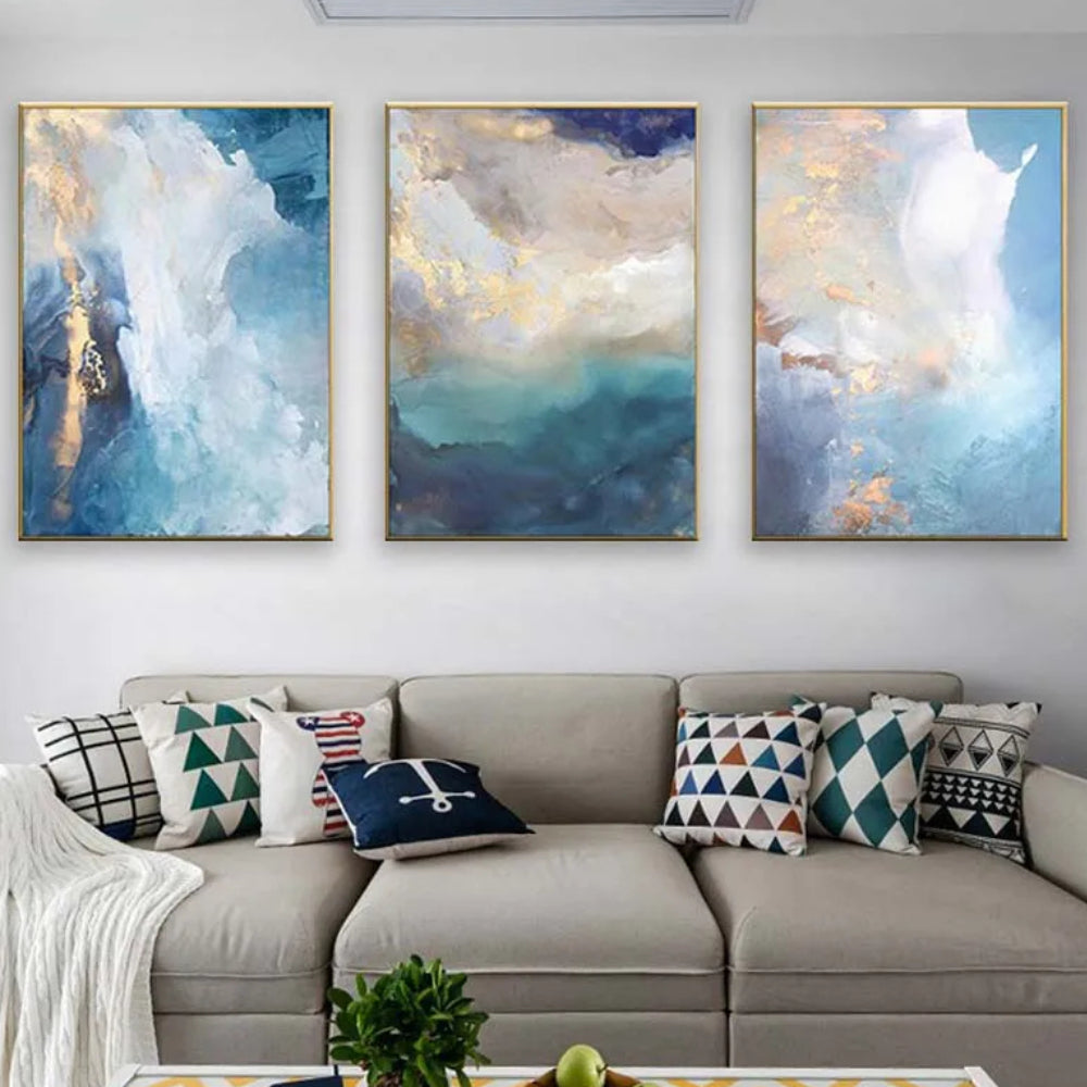 Room mockup showing three abstract panels with cloudy white and pale blue fields, deep teal areas and gold-coloured accents.