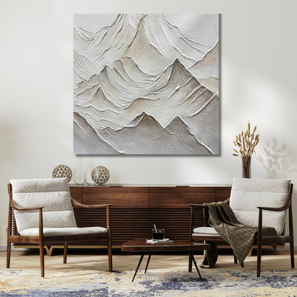 A textured mountain painting in beige, white, and gray tones displayed above a console table in a room with two armchairs and a wooden floor.