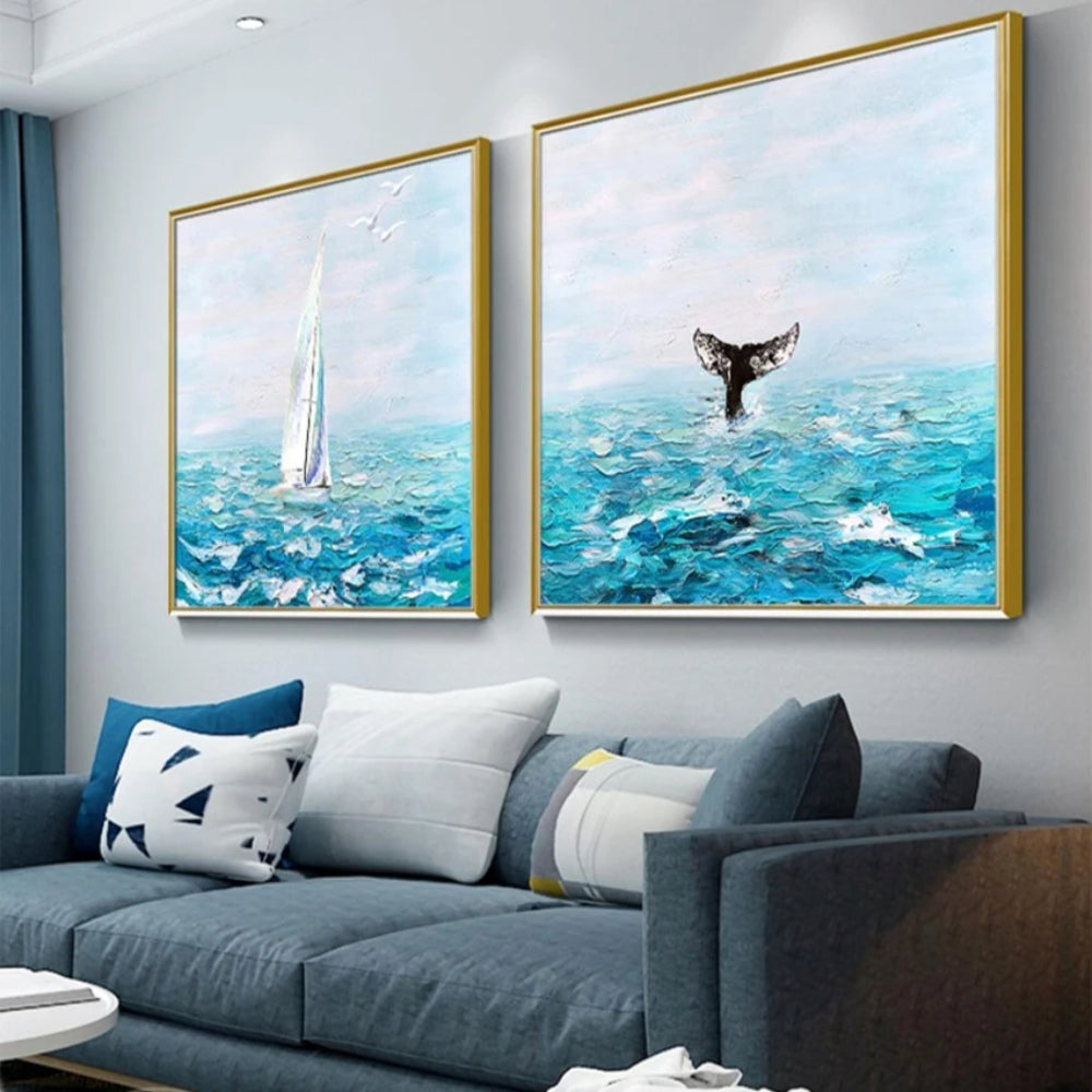 Room mockup showing pair of turquoise seascapes with a tall white sailboat and a dark whale tail beneath pale blue skies.