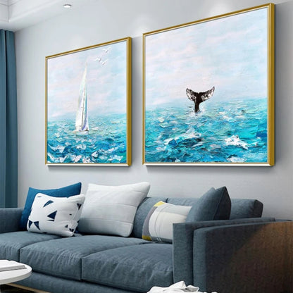 Room mockup showing pair of turquoise seascapes with a tall white sailboat and a dark whale tail beneath pale blue skies.