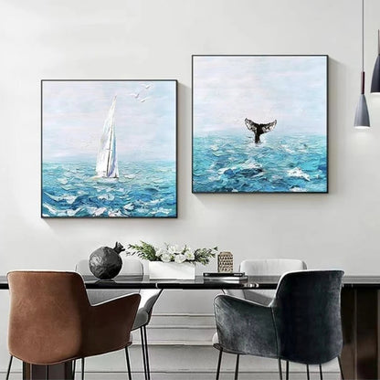 Room mockup showing pair of turquoise seascapes with a tall white sailboat and a dark whale tail beneath pale blue skies.
