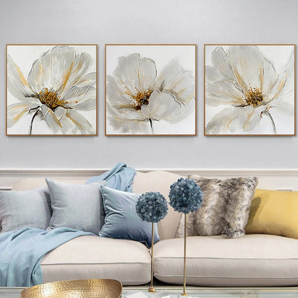 Room mockup showing three white flower paintings with fine grey petal outlines and gold-coloured centres on pale backgrounds.