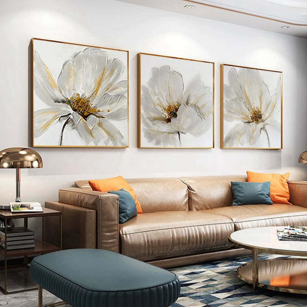 Room mockup showing three white flower paintings with fine grey petal outlines and gold-coloured centres on pale backgrounds.