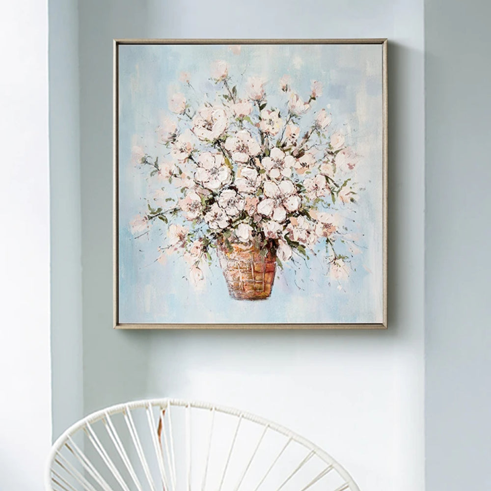 Room mockup showing small white and pale pink blossoms clustered on slender branches in a brown vase against pale blue.