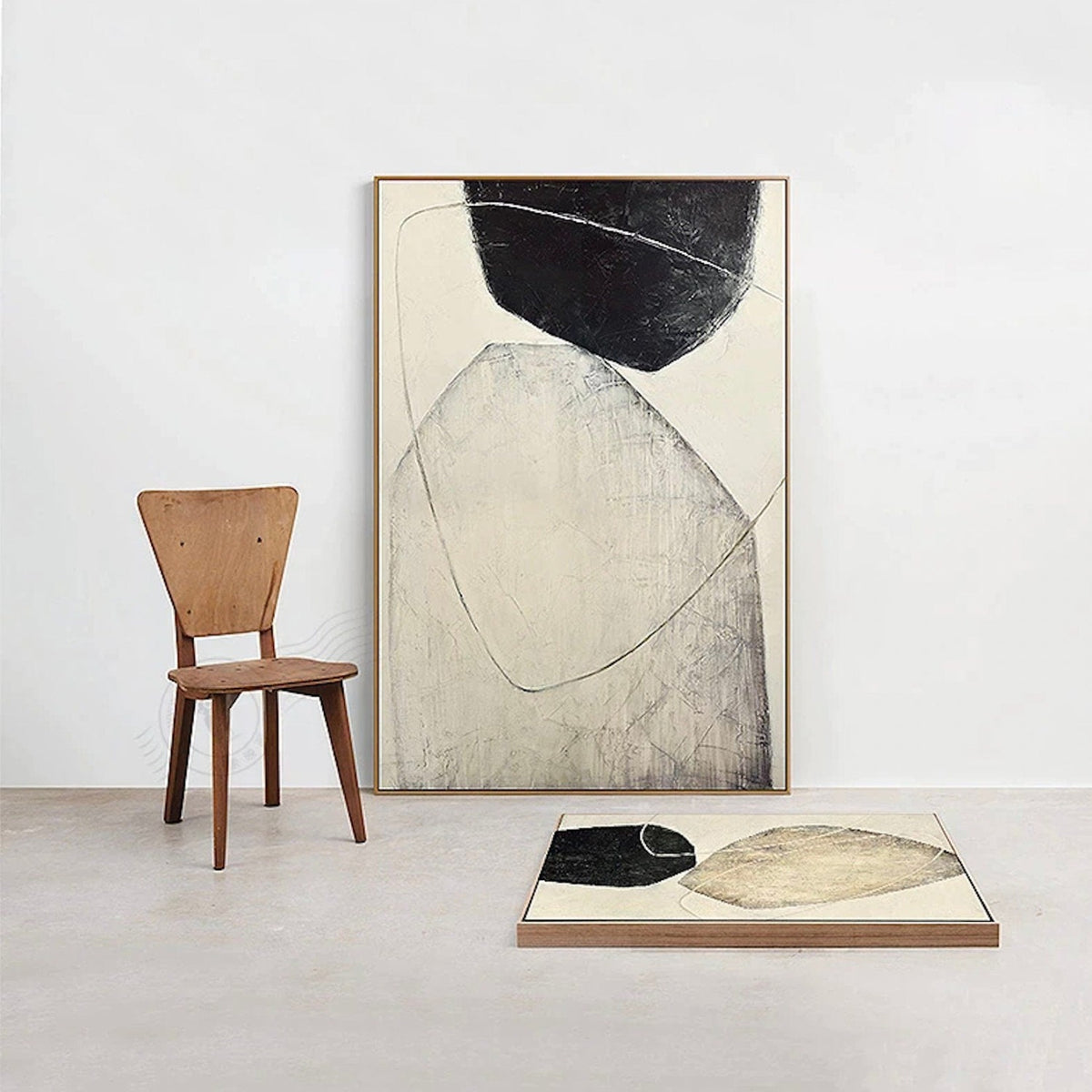 Room mockup. Complementary beige and black rounded abstract forms shown in a tall leaning frame and a second canvas laid below.