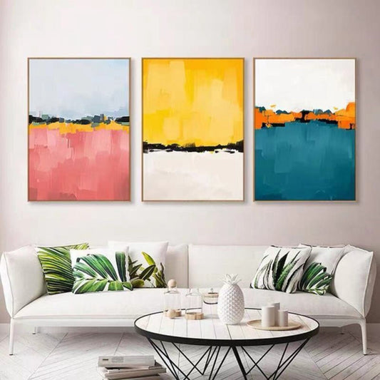 Room mockup. Three-panel abstract artwork with pink, yellow and teal fields divided by narrow dark horizon-like bands.