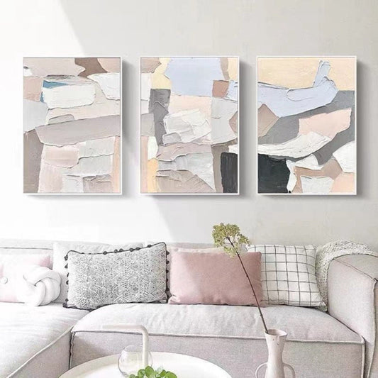Room mockup. Three-panel abstract artwork with layered-looking white, grey, blush and pale yellow irregular blocks.